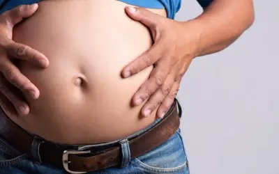 Un homme, je suis mince avec un gros ventre, tient son abdomen proéminent au-dessus de son jean et de sa ceinture.