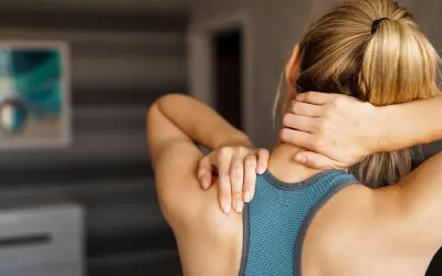 Femme se tenant le cou et le haut du dos, ressentant une douleur. La signification de cette douleur peut varier.