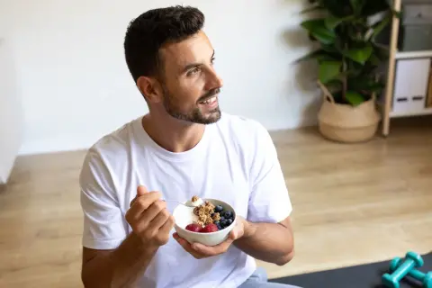 Un jeune intermittent savoure un bol de yaourt grec avec des fruits rouges et du granola, prêt pour sa journée.