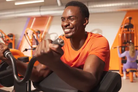 Un homme souriant s'entraîne pour muscler les bras sur une machine de musculation.