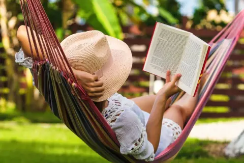 Une personne lit un livre dans un hamac coloré, profitant d'un des 7 types de repos sous un chapeau de paille.