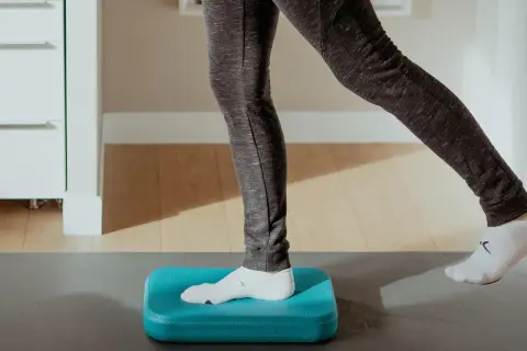 Exercice d'équilibre sur un coussin bleu pour améliorer la proprioception cheville.