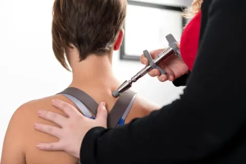 Thérapeute utilisant un appareil pour soulager la douleur haut du dos gauche d'une patiente.