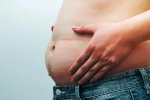 Une main touche un ventre proéminent, soulevant la question : le pain complet fait-il grossir le ventre ?
