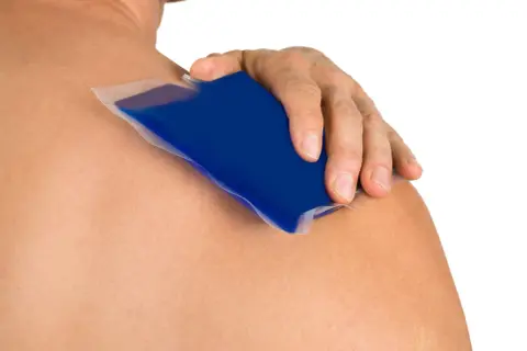 Main d'une personne appliquant une poche de glace bleue sur son épaule pour soigner une tendinite.