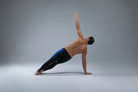 Homme en planche latérale, bras levé, pour perdre poignée d'amour. Musculature dorsale et abdominale visible.