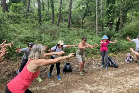 Groupe pratiquant le shinrin yoku en forêt, bras tendus, profitant de la nature.