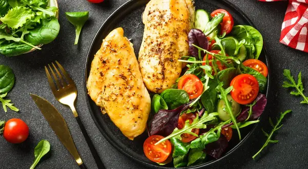 Deux blancs de poulet grillés avec une salade colorée, un repas sain parmi les 10 meilleurs aliments anti-cholestérol.