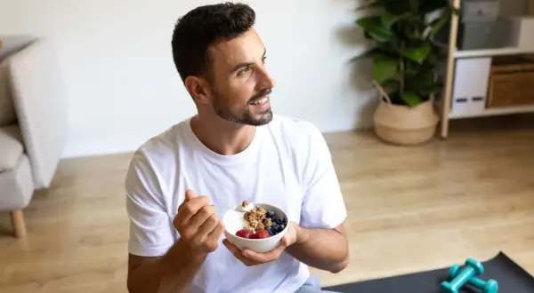 Un jeune intermittent savoure un bol de yaourt grec avec des fruits rouges et du granola, prêt pour sa journée.