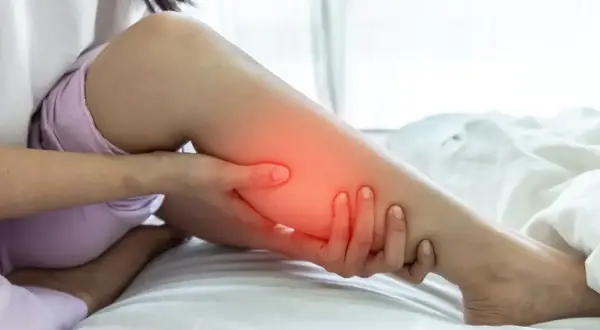 Une personne se tient la jambe, une zone rouge vif sur le mollet indiquant une douleur.