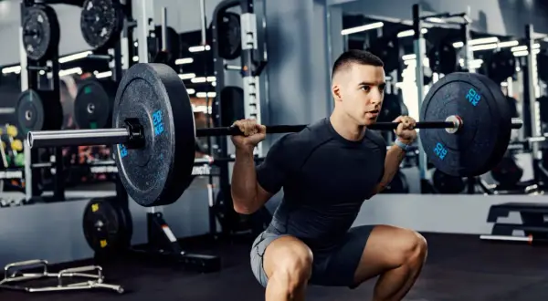 Un homme fait un squat avec une barre chargée, un exercice clé pour un programme musculation prise de masse.