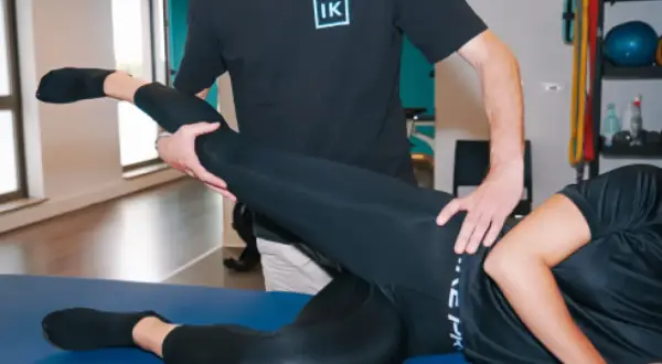 Un kinésithérapeute aide une patiente à étirer sa jambe, soulageant potentiellement un nerf coincé hanche symptôme.