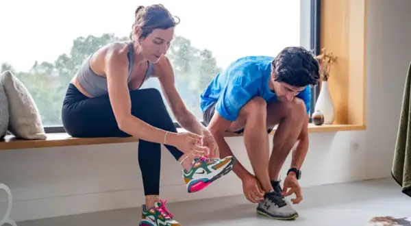 Un couple se prépare pour son programme de remise en forme, attachant ses chaussures de sport près d'une grande fenêtre.