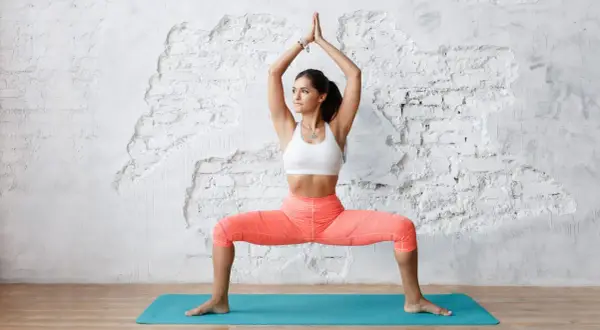Une femme en tenue de sport pratique le yoga, bras levés, jambes écartées. Une belle posture pour comprendre pourquoi pratiquer le yoga.