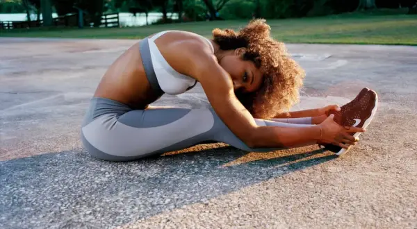 Femme en tenue de sport pratiquant une posture de yoga anti-stress, étirant ses jambes sur un sol extérieur.