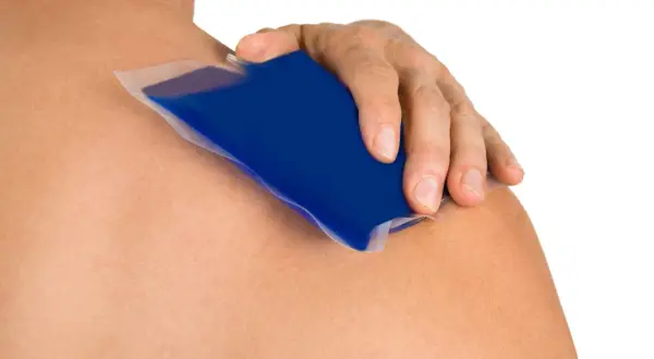 Main d'une personne appliquant une poche de glace bleue sur son épaule pour soigner une tendinite.