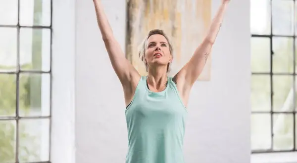 Femme aux bras levés, profitant d'un moment pour calmer son mental. La lumière naturelle baigne la pièce, accentuant sa sérénité.