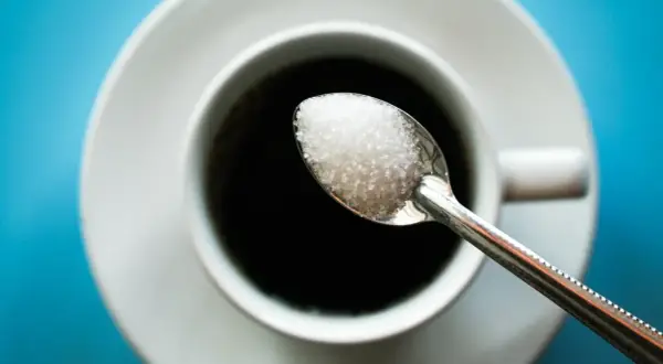 Cuillère de sucre au-dessus d'une tasse de café noir. Une image pour illustrer l'arrêter le sucre effet.