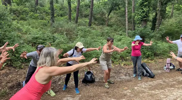 Groupe pratiquant le shinrin yoku en forêt, bras tendus, profitant de la nature.