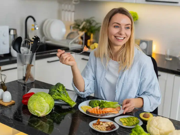 Femme souriante dégustant un menu équilibré pour perdre du poids : saumon, brocolis, avocat, noix et légumes frais.